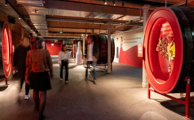 Besucher in einer Markenausstellung mit beleuchteten Fässern